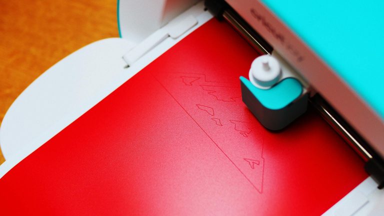 Close-up of a cutting machine engraving a pattern on red paper indoors.